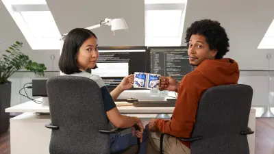 Dois associados à secretária em frente aos seus monitores numa sessão de programação a dois e a brindar com as canecas